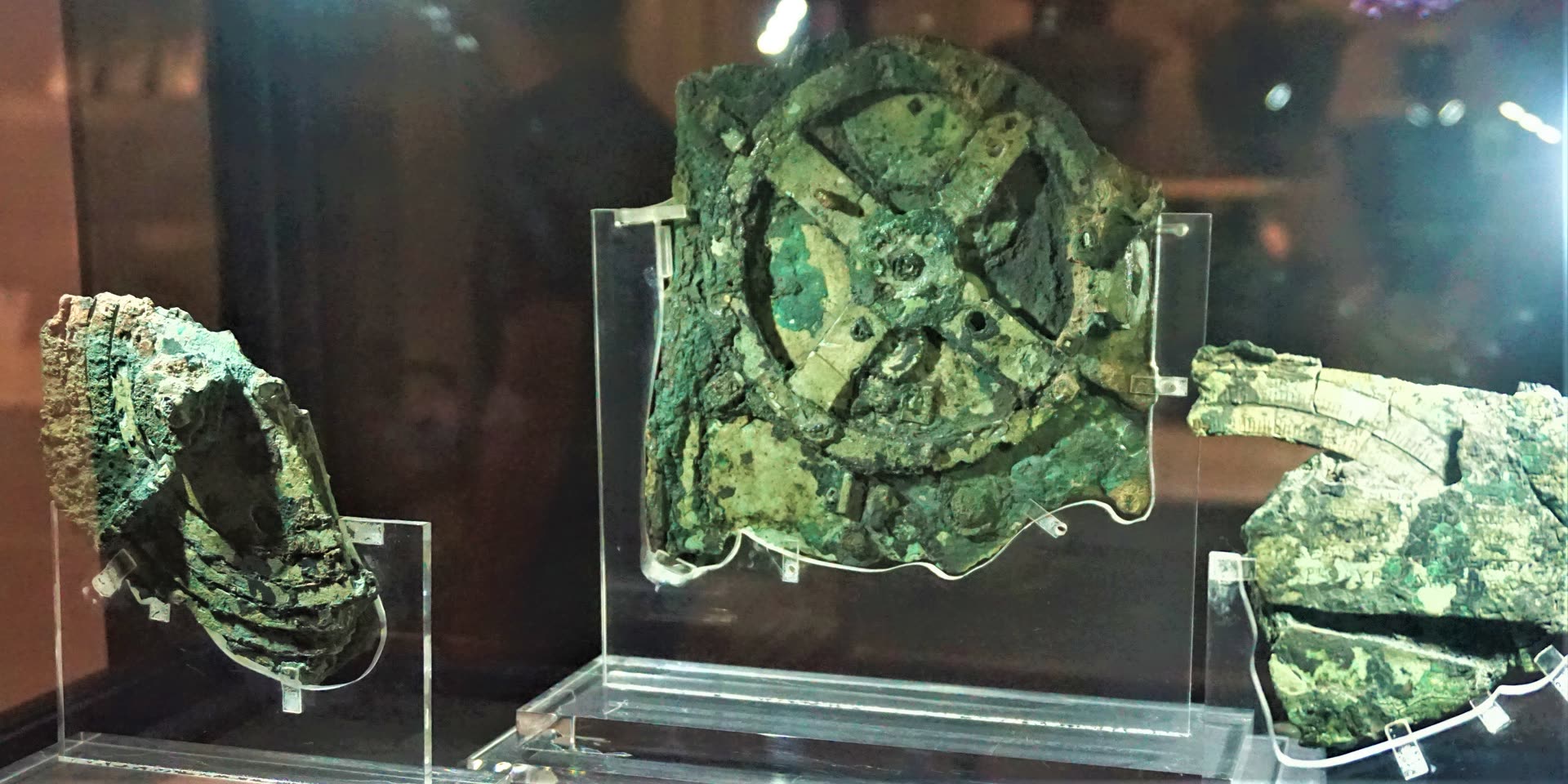 The corroded bronze fragments of the Antikythera Mechanism, including the large four-spoked main drive gear of Fragment A, on display at the National Archaeological Museum, Athens