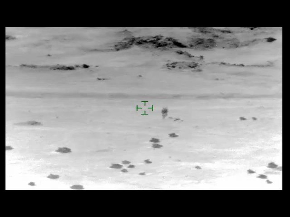 Actual thermal frame from the AARO-released Al Taqaddum Object video, showing the dark, elongated thermal signature at center frame with the sensor's green targeting reticle nearby, against a gray desert landscape