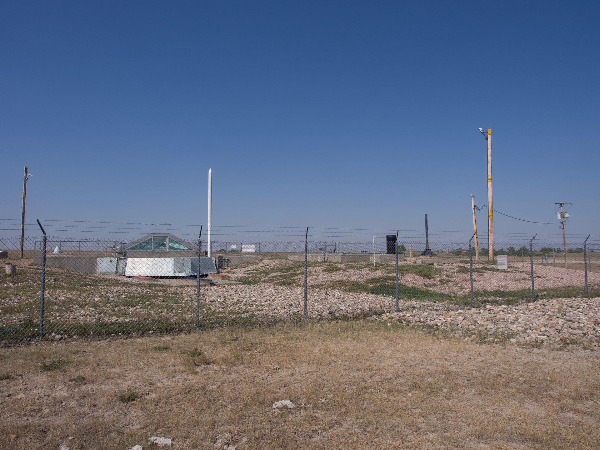 A fenced, unmanned Minuteman II launch facility on the South Dakota plains, with the silo's closed blast door, security fencing and antenna mast visible